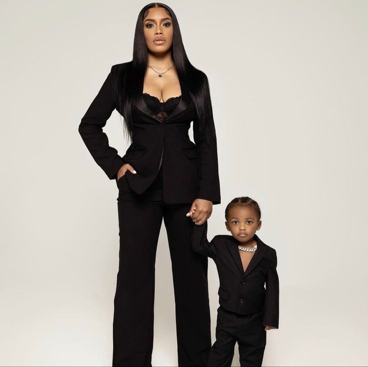 a woman in a black suit standing next to a small child