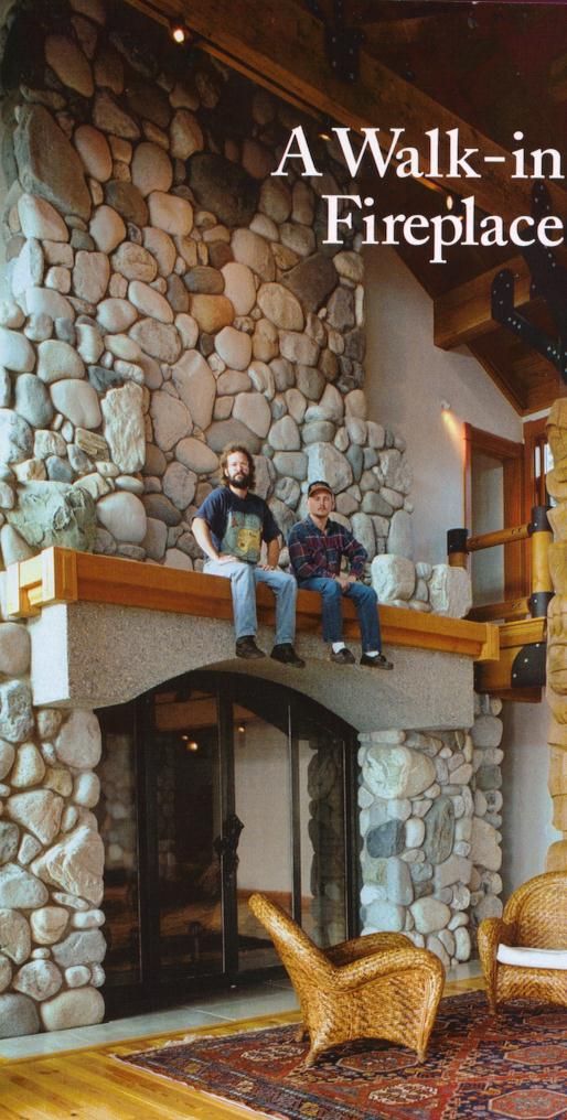 two men sitting on the ledge of a fireplace in a living room with stone walls