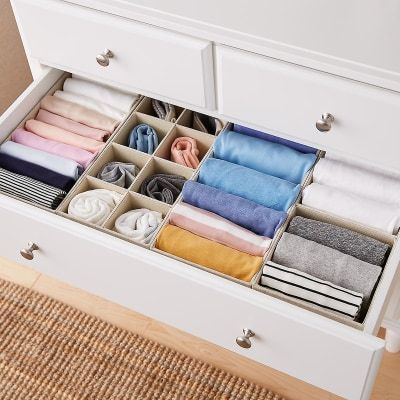 an open drawer with several pairs of folded clothes in it on a carpeted floor