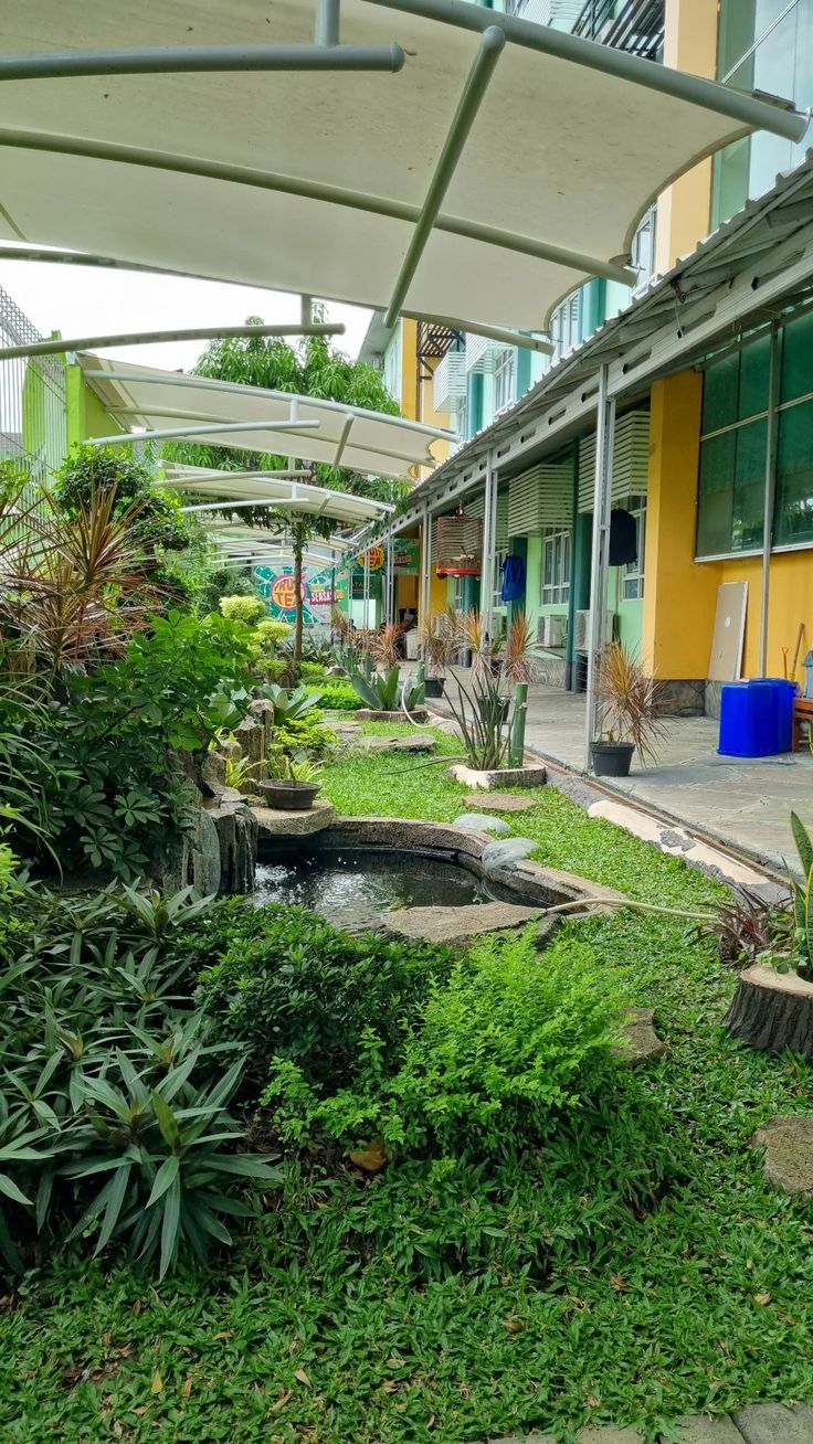 an outdoor area with lots of green plants and trees in front of a yellow building