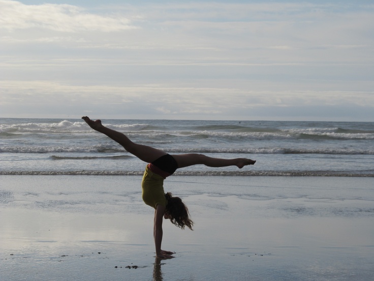 a woman doing a handstand on the beach