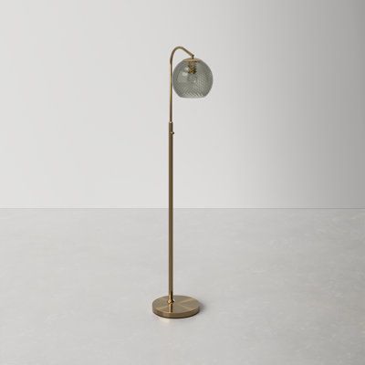 a floor lamp with a glass shade on the top and an iron base, standing on a white surface