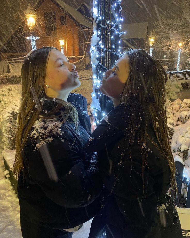 two women standing next to each other in front of a christmas tree with lights on it