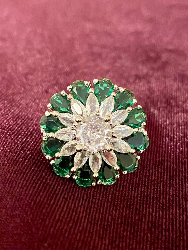 a green and white brooch sitting on top of a red velvet covered tablecloth