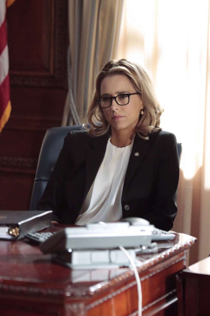 a woman sitting at a desk in front of an american flag