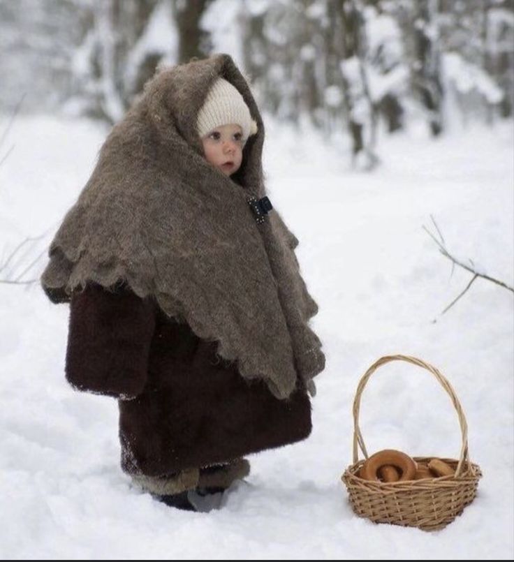 a little boy dressed up like a bear in the snow next to a wicker basket