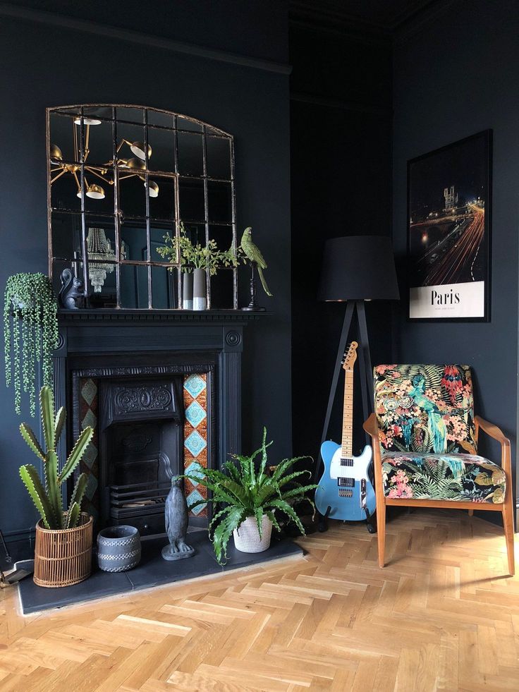 a living room with black walls and wooden flooring, potted plants on the fireplace mantel