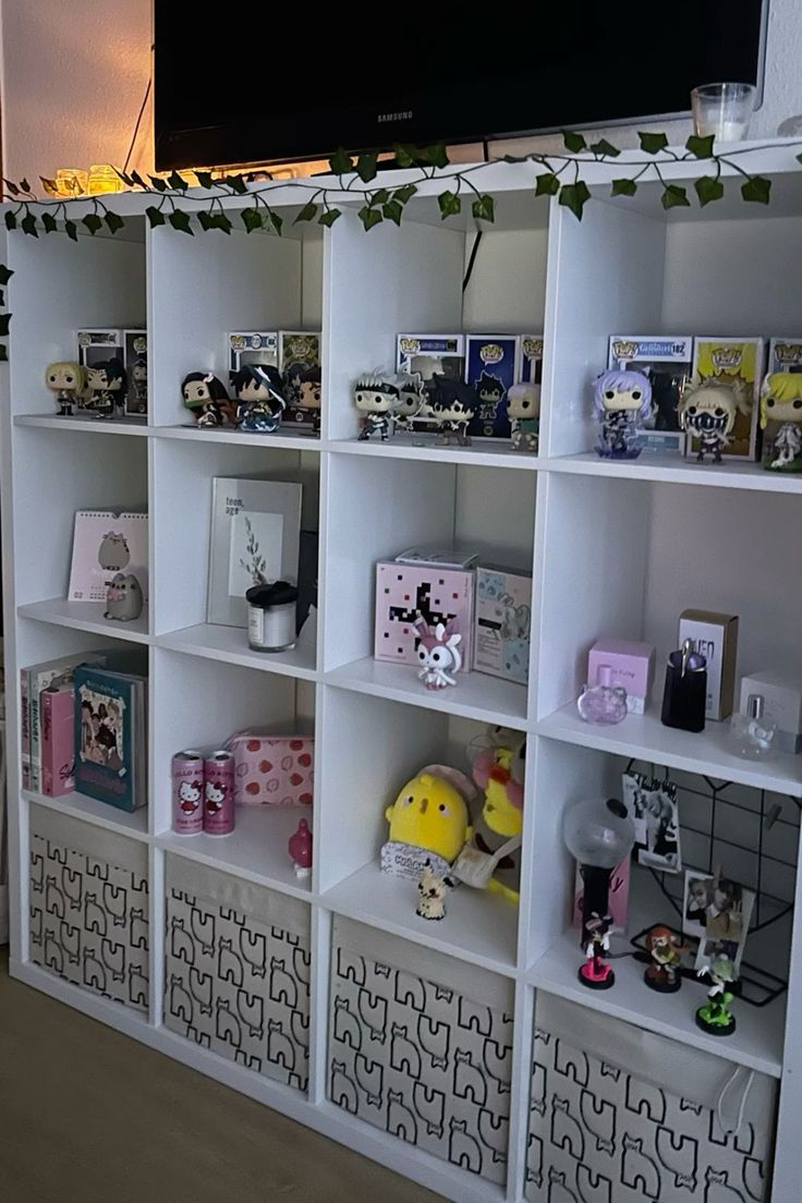 a television mounted on top of a white book shelf filled with toys and figurines