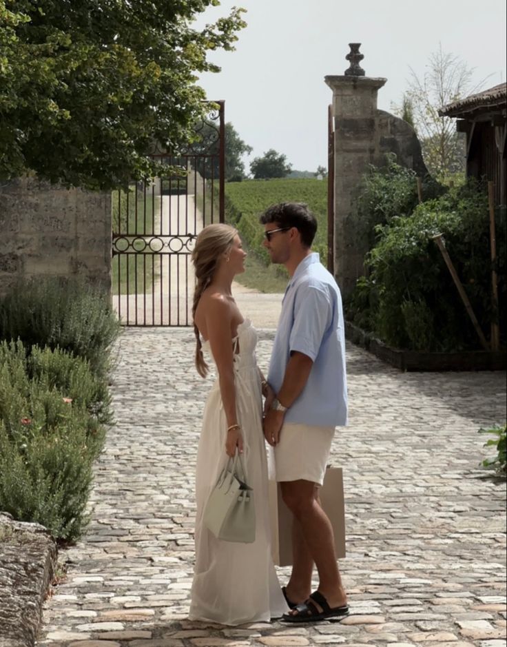 a man and woman are standing in front of an iron gate on a cobblestone walkway