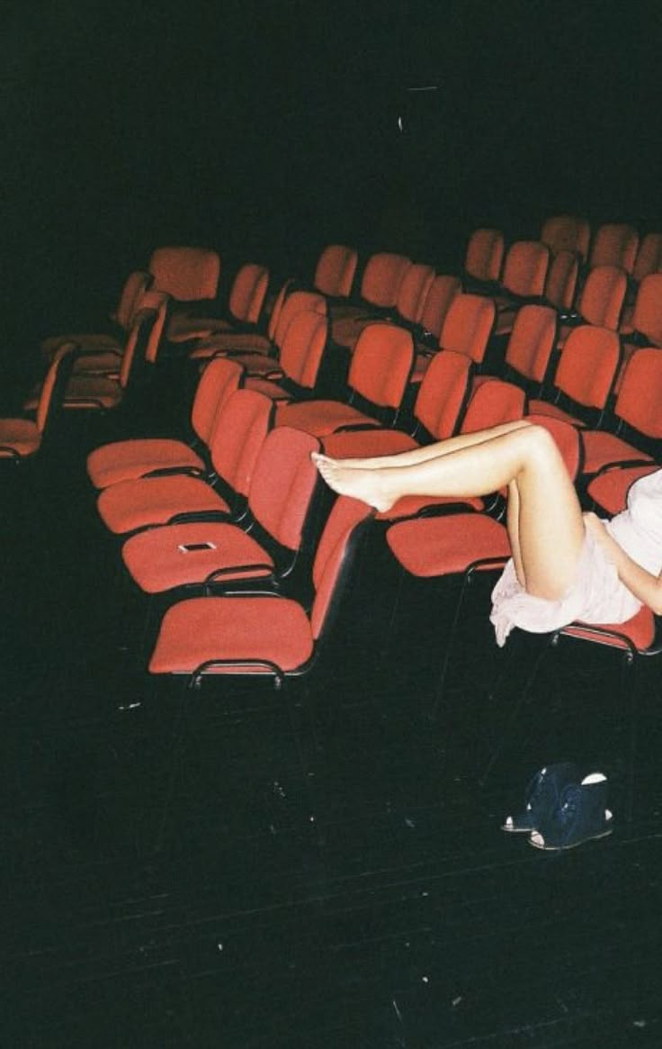 a woman laying on top of a red chair in front of an empty theater seat