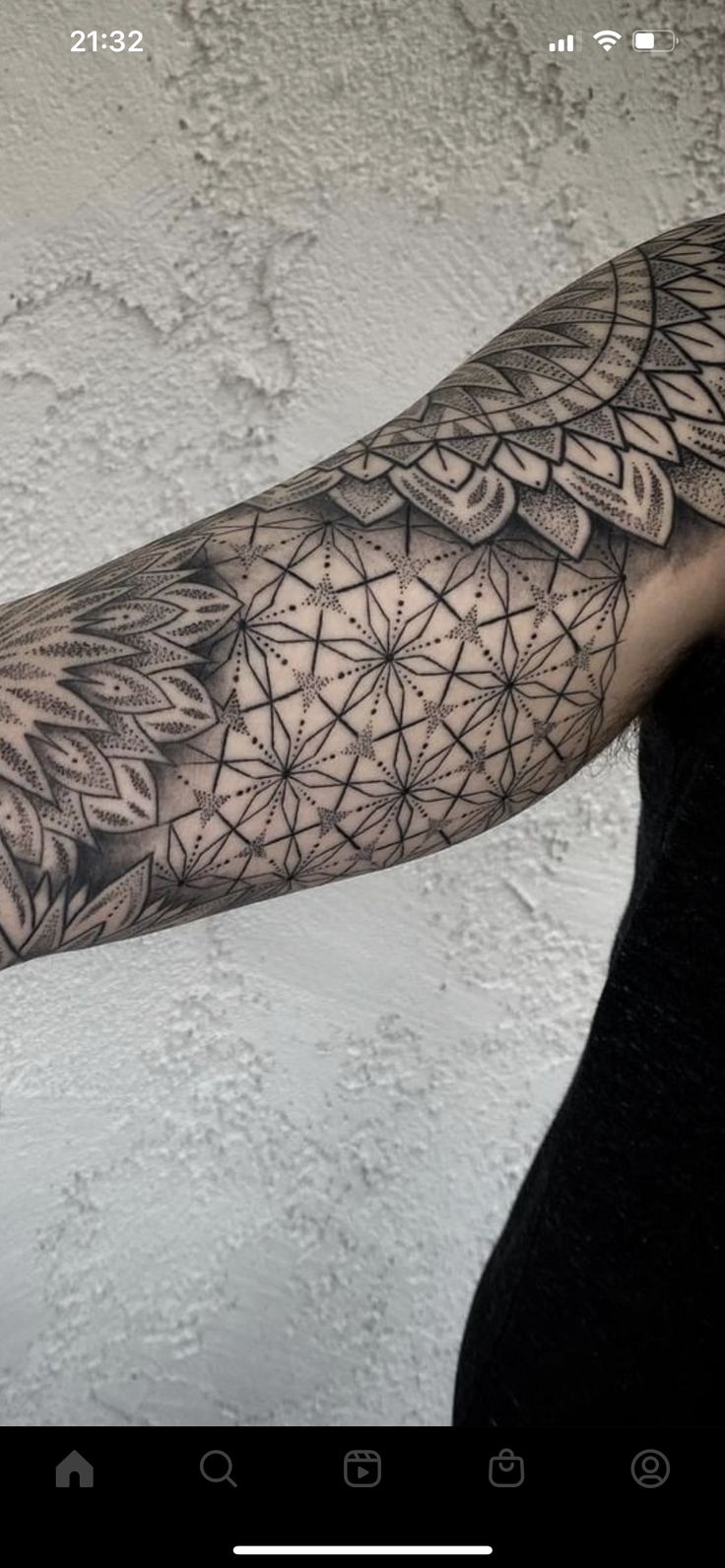 the arm is covered in intricate black and white tattoos, with geometric designs on it