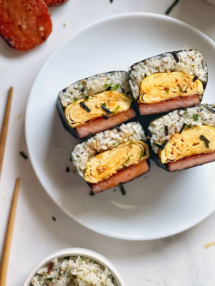 four pieces of sushi on a white plate with chopsticks next to it