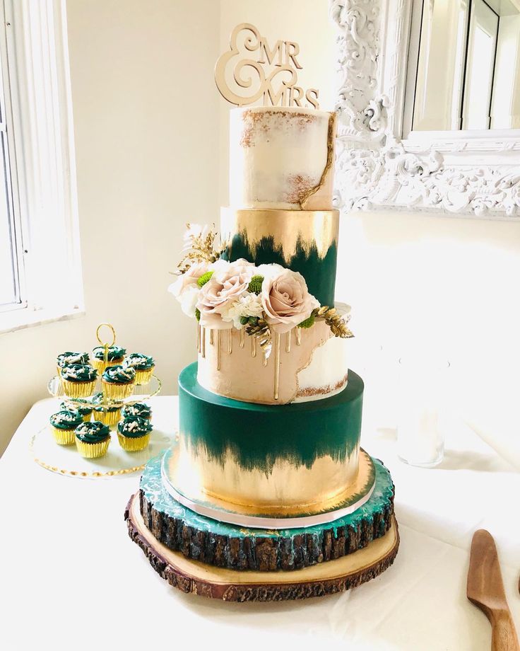 a three tiered cake sitting on top of a table next to cupcakes