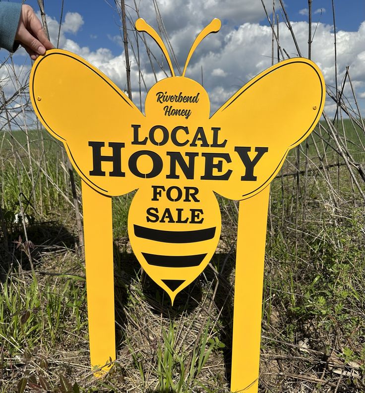 a yellow sign that says local honey for sale in front of some grass and blue sky