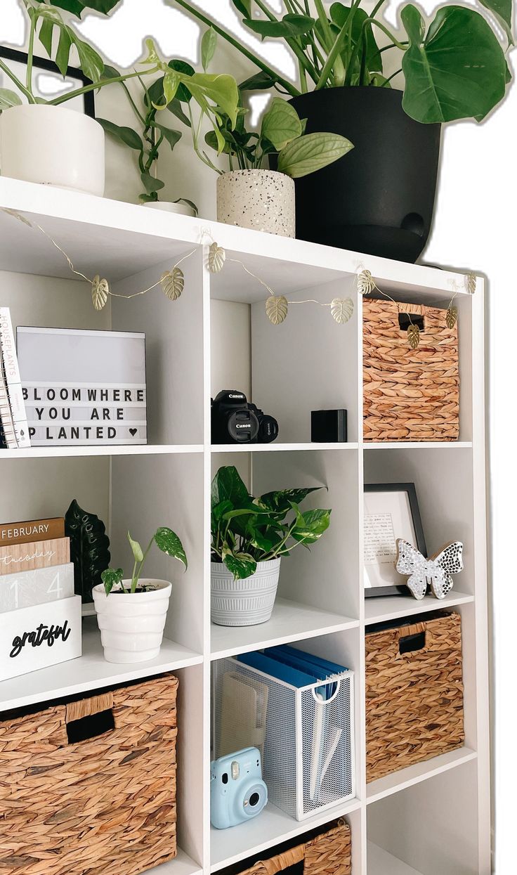 a white bookcase with baskets and plants on the top, along with other items