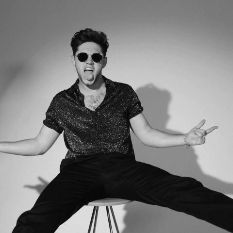 a man sitting on top of a stool with his hands in the air while wearing sunglasses