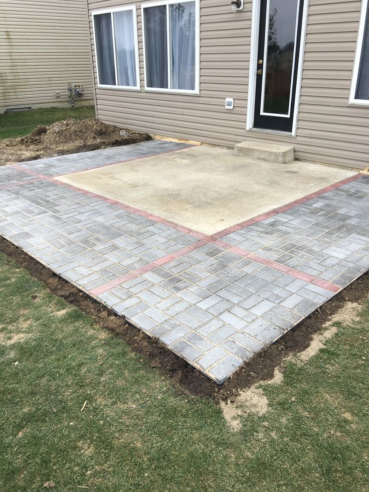 a brick patio being built in front of a house with grass and dirt around it