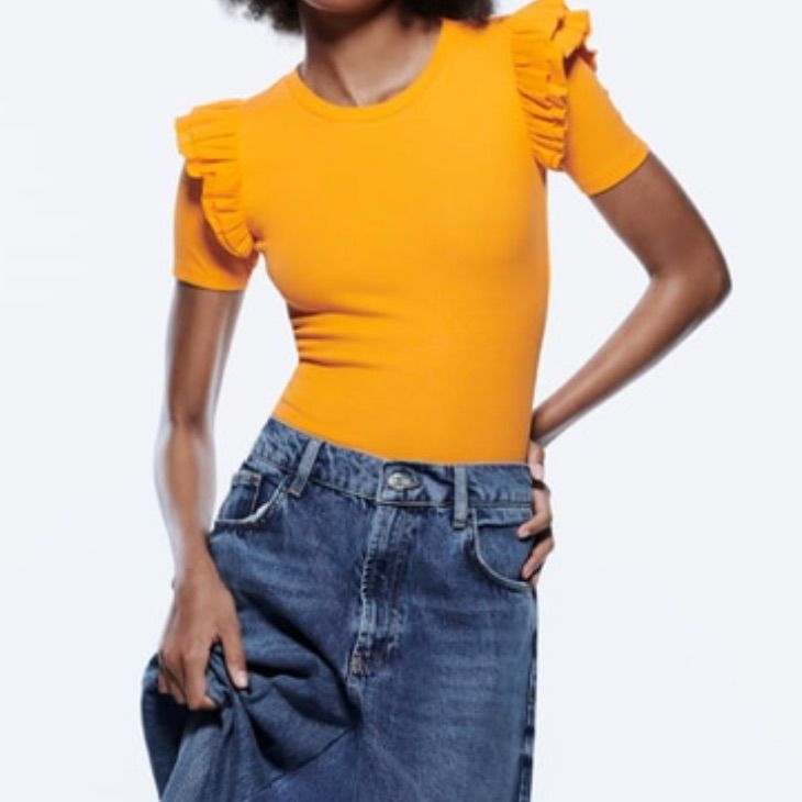 a woman in an orange top and denim skirt