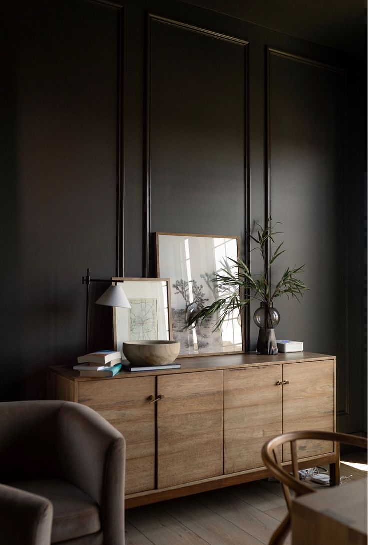 a living room with black walls and wooden furniture in the corner, along with a potted plant on top of a dresser