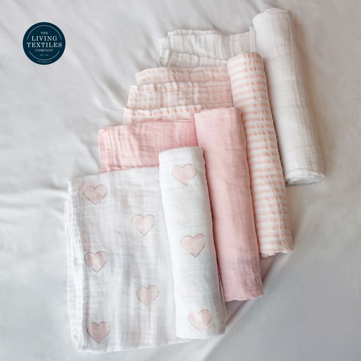 five baby swaddles laid out on top of a white bed with pink hearts