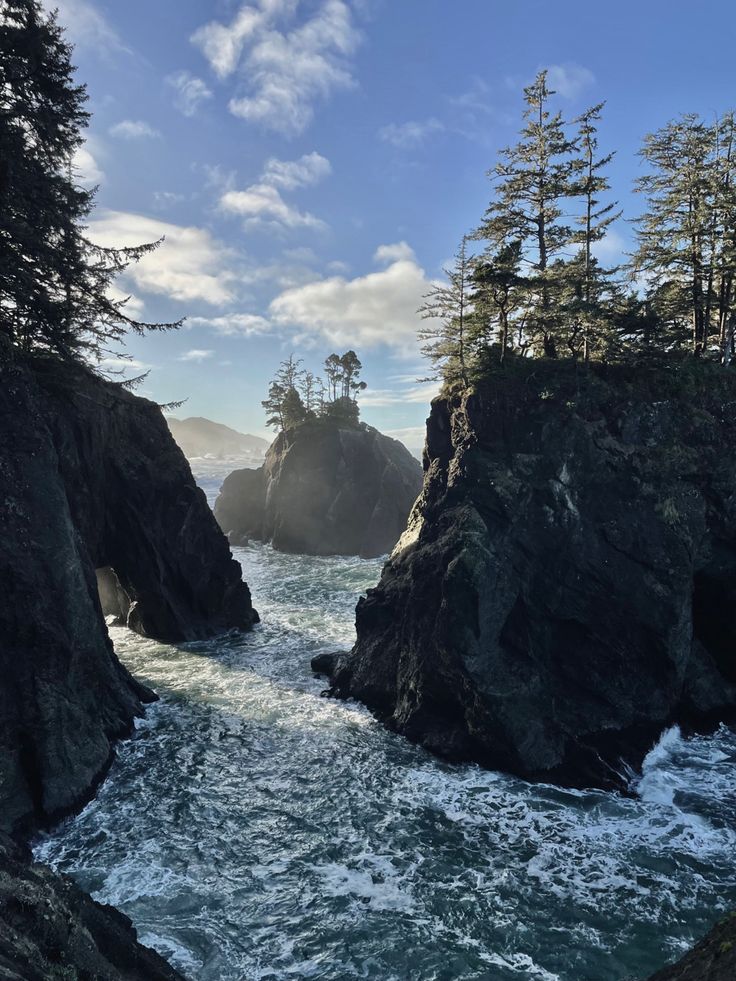 the water is rushing between two large rocks in the middle of an ocean with pine trees on both sides