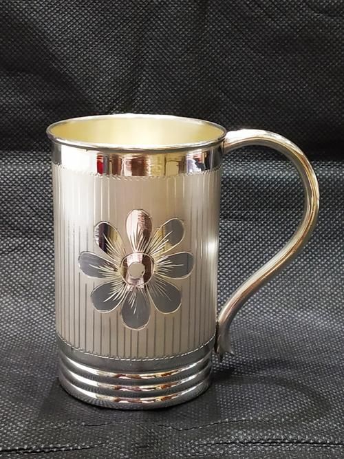 a silver coffee mug with a flower design on the front and sides, sitting on a black background