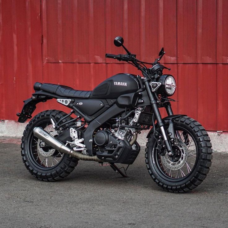 a black motorcycle parked in front of a red building with the word yamaha on it