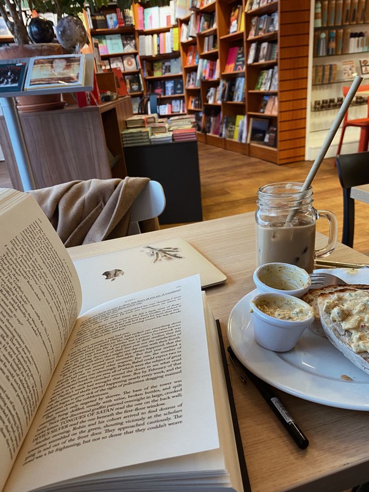 an open book sitting on top of a table next to a plate with food and drink