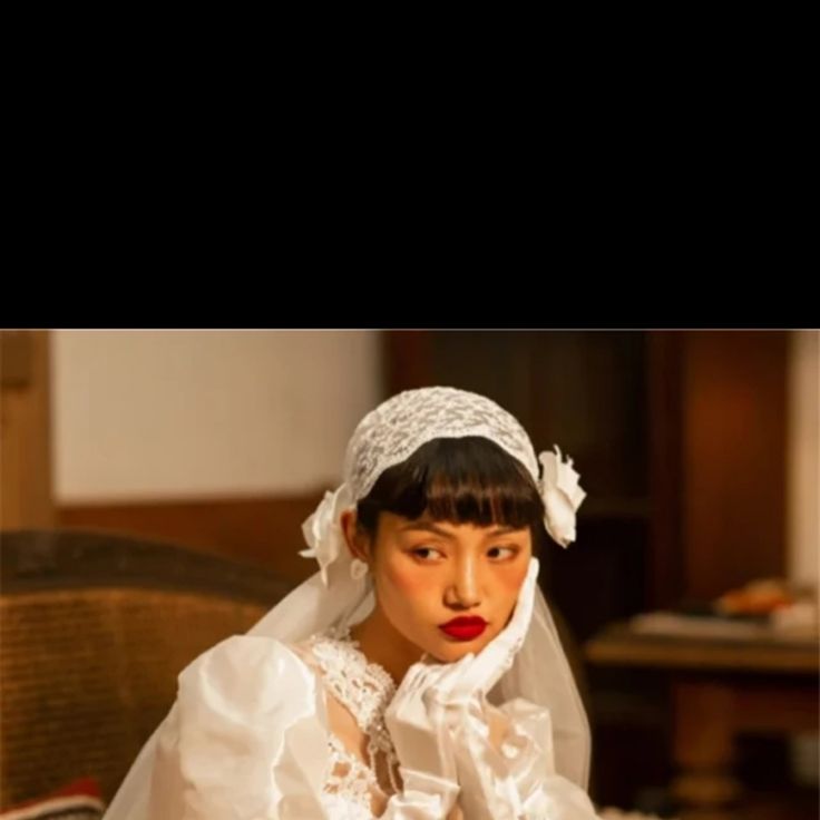 a woman in a white wedding dress sitting on a chair with her hands folded over her face