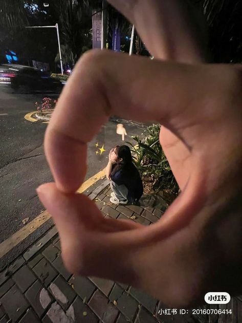 a person sitting on the ground with their hand in front of them, making a heart shape