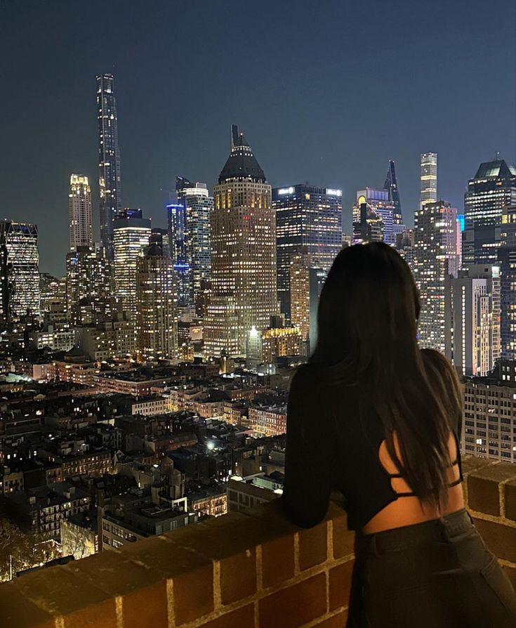 a woman standing on top of a brick building looking at the city lights in the distance