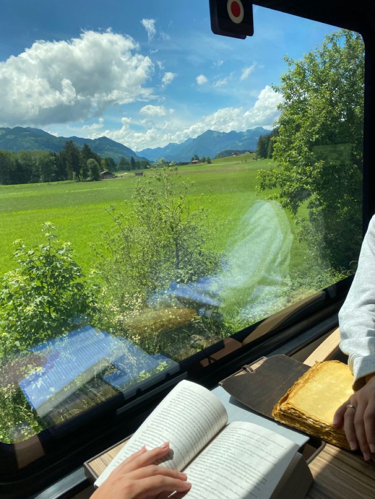 a person sitting at a table with an open book in front of them, looking out the window