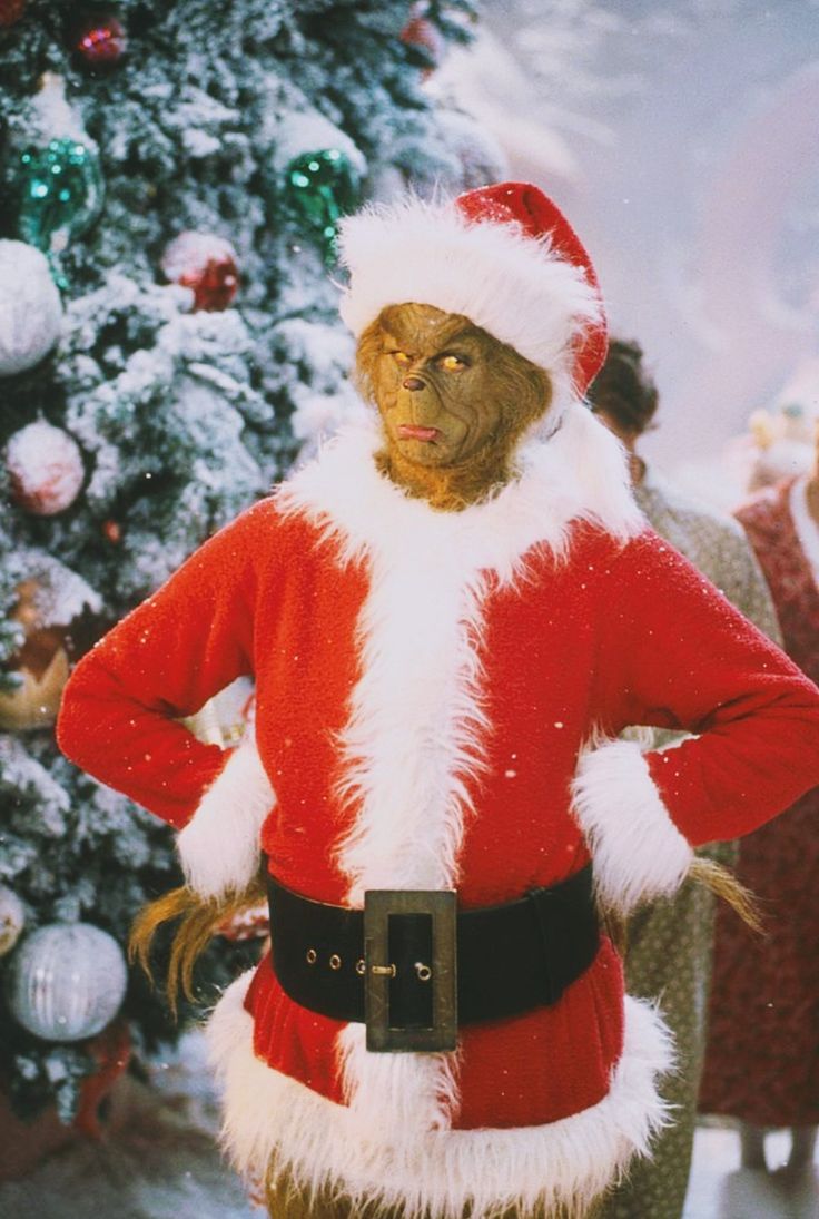 a man dressed as santa clause standing in front of a christmas tree