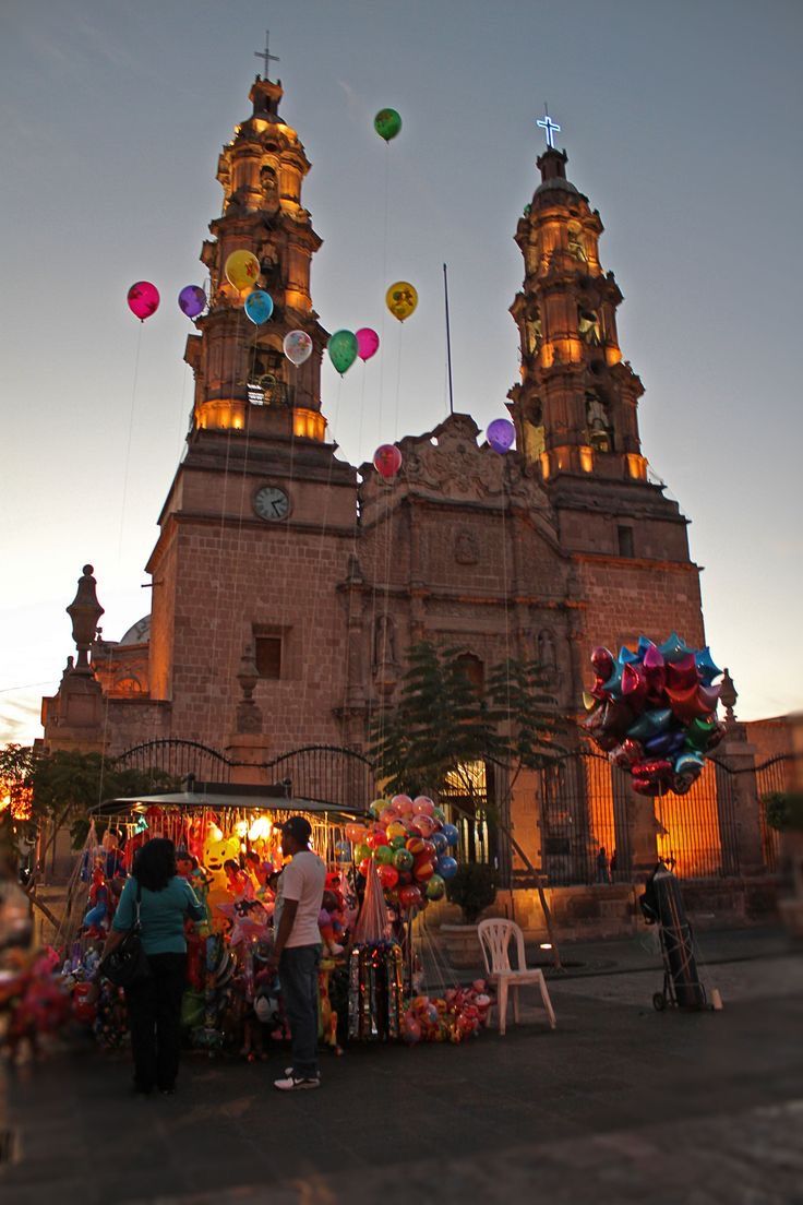 an old church with balloons in the air and people walking around it at night time