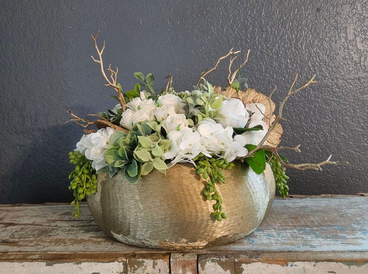 a vase filled with white flowers sitting on top of a wooden table next to a gray wall