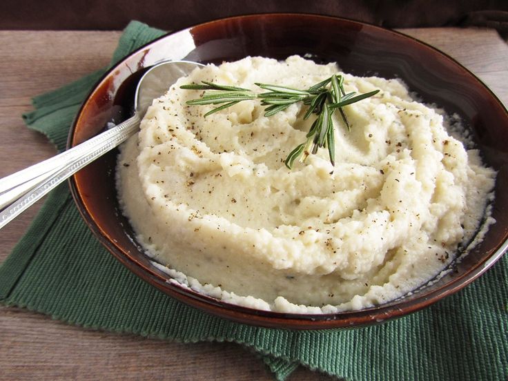 mashed potatoes in a brown bowl with a sprig of rosemary