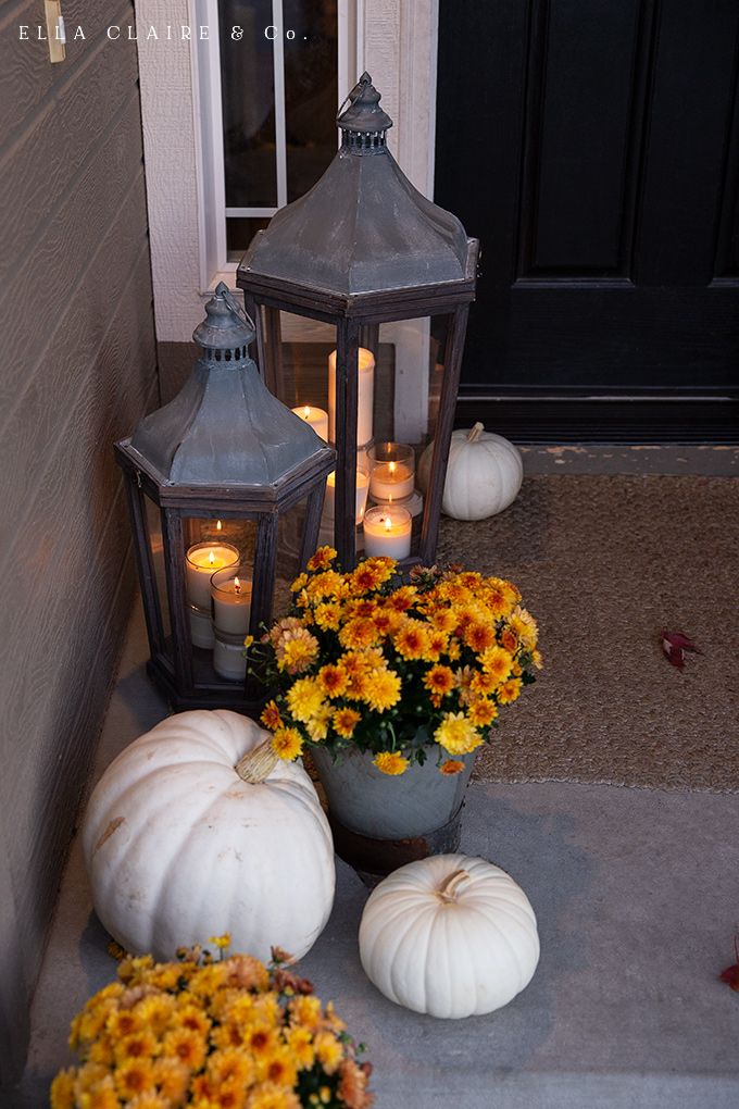 some pumpkins and flowers are sitting on the front porch with lanterns in the background