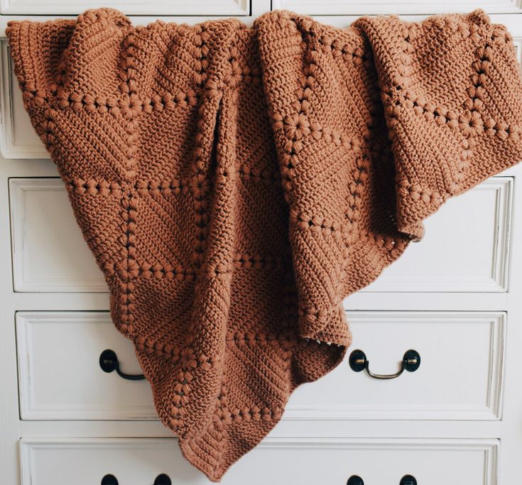 a brown knitted blanket hanging on a white dresser