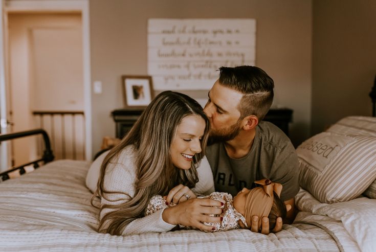 a man and woman laying on top of a bed next to each other holding a baby