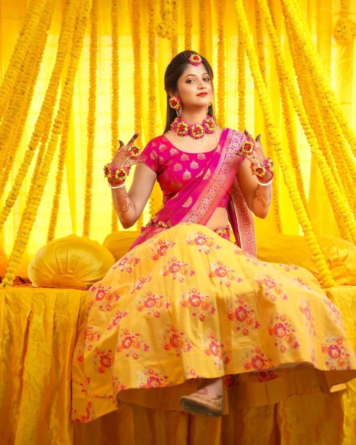 a woman sitting on top of a bed wearing a pink and yellow sari dress