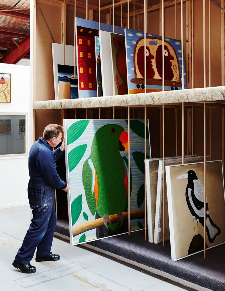 a man looking at paintings on display in a room with wooden shelves and shelving