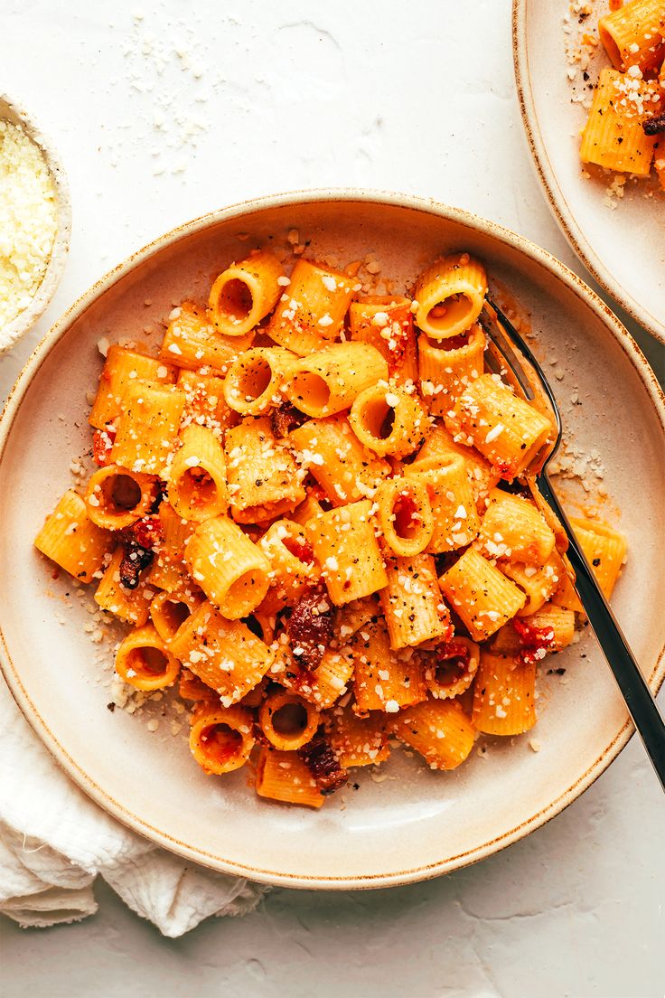 two plates filled with pasta and sauce on top of a white table next to a spoon