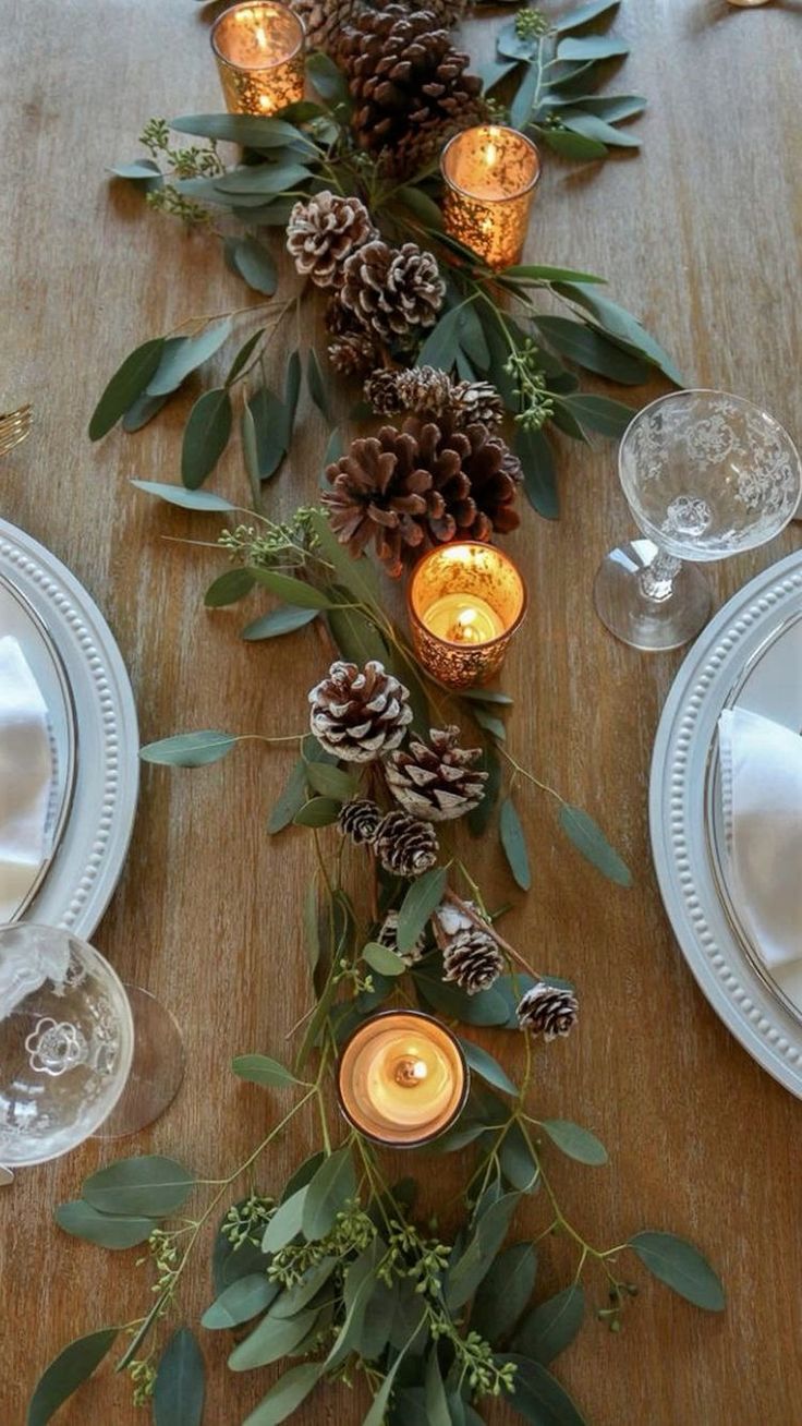 the table is set with pine cones, greenery and candles