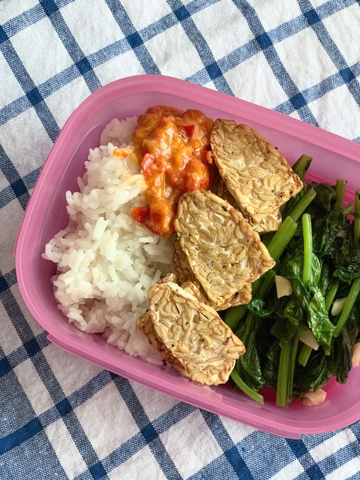 a pink plastic container filled with rice and meat covered in sauce next to broccoli