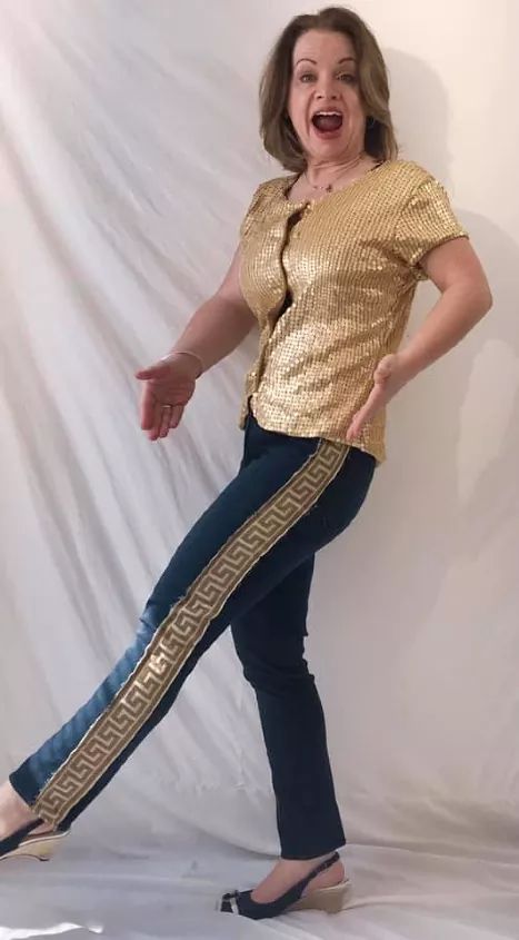 a woman in gold shirt and jeans posing for the camera