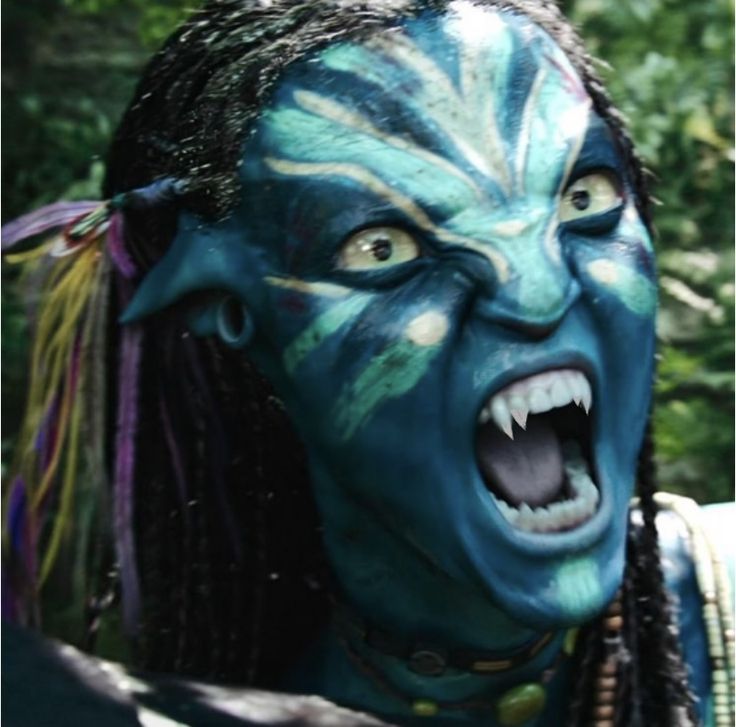 a woman with blue paint on her face and mouth is making an angry face as she stands in front of trees