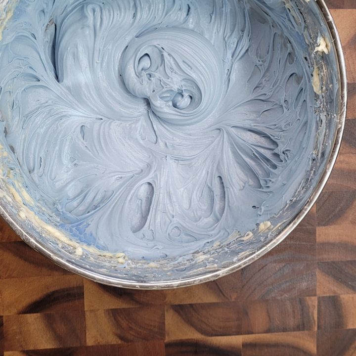 a wooden table with a metal bowl filled with blue icing on top of it