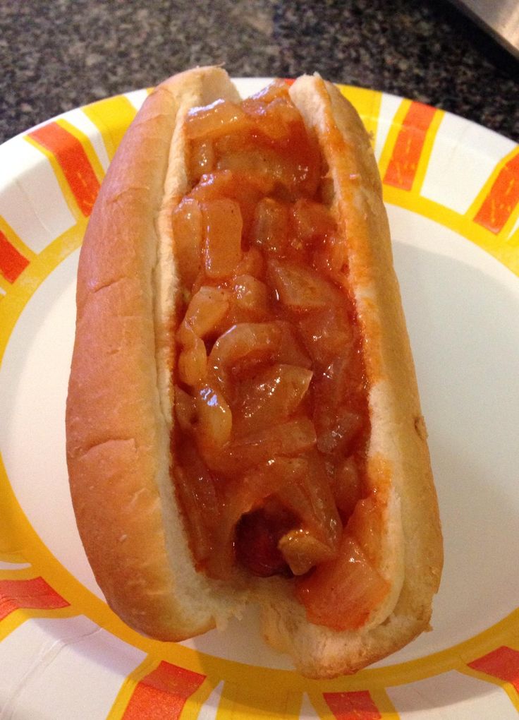 a hot dog on a bun covered in onions and ketchup sitting on a paper plate