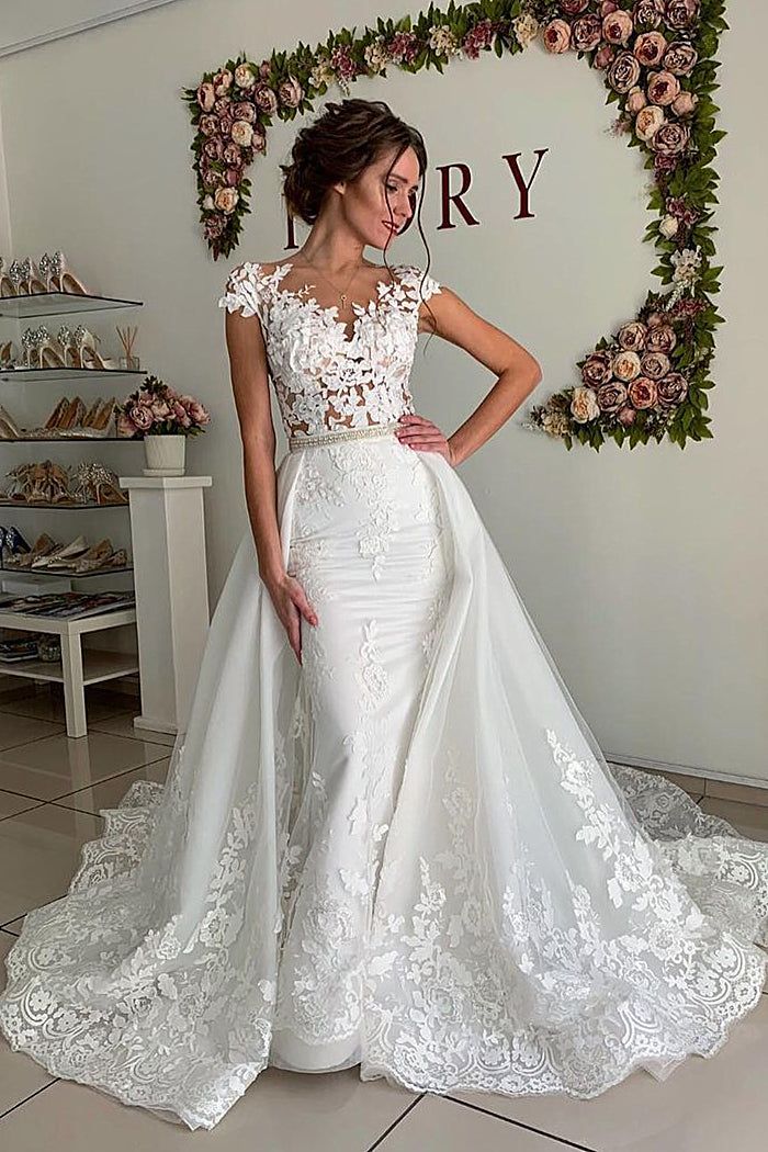 a woman standing in front of a floral wall wearing a wedding dress with an open back