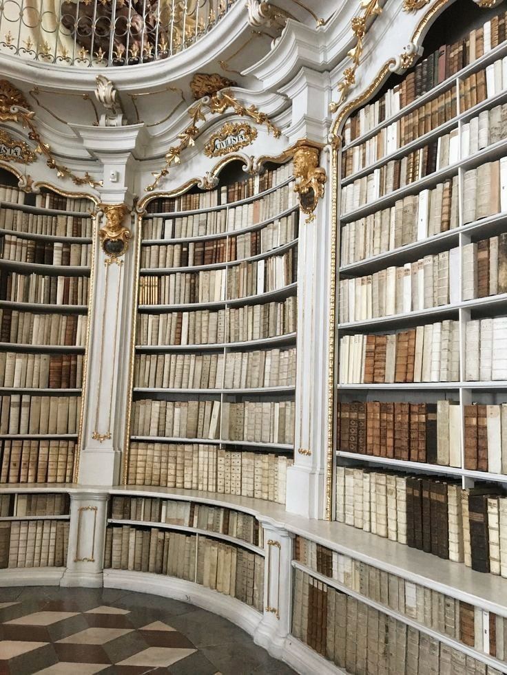 a room filled with lots of books and gold trimmings on the walls next to a spiral staircase